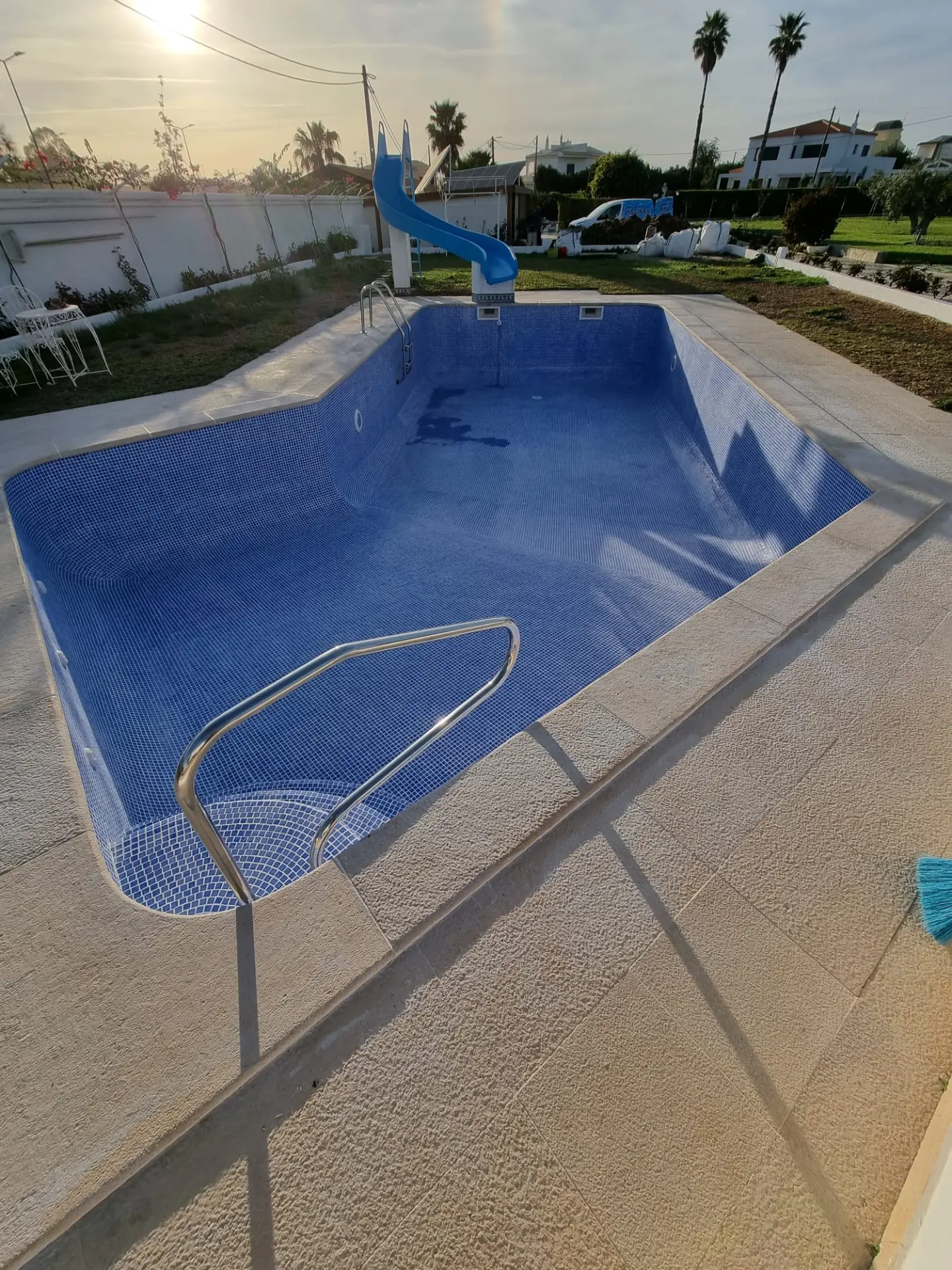 Piscina renovada com água azul e escorrega ao pôr do sol
